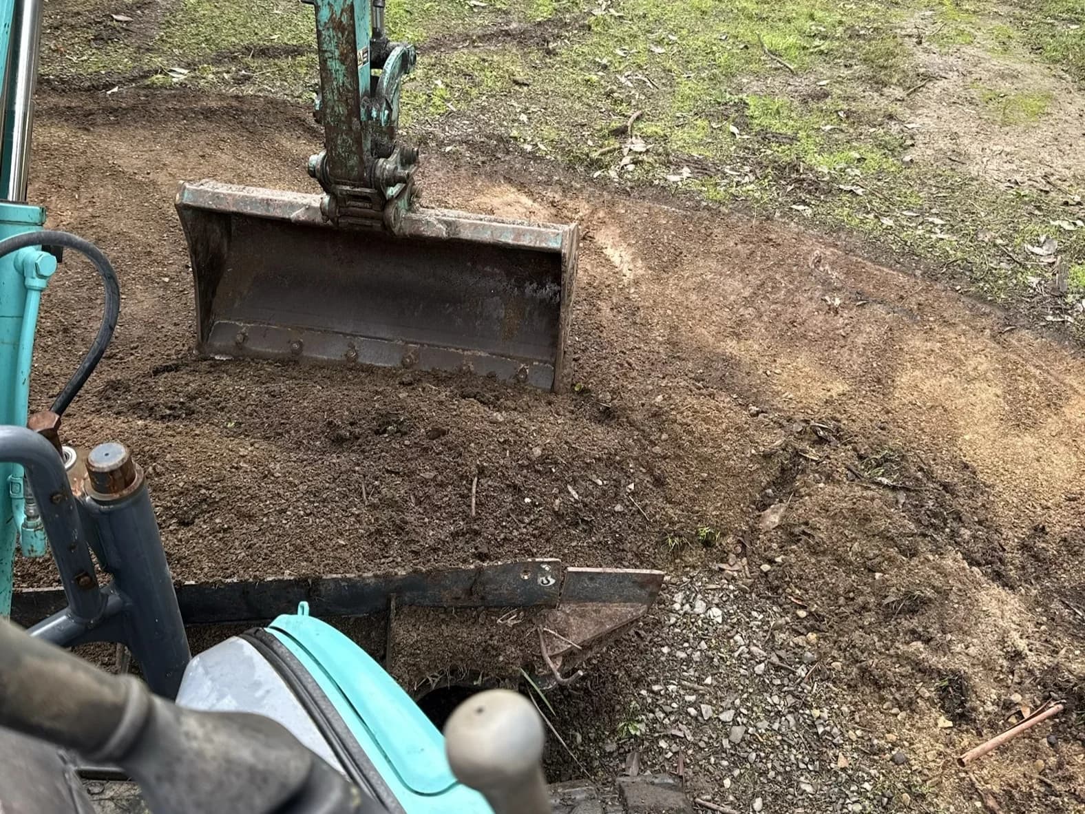 A mini excavator cutting a batter into sloped ground beside a gravel drive