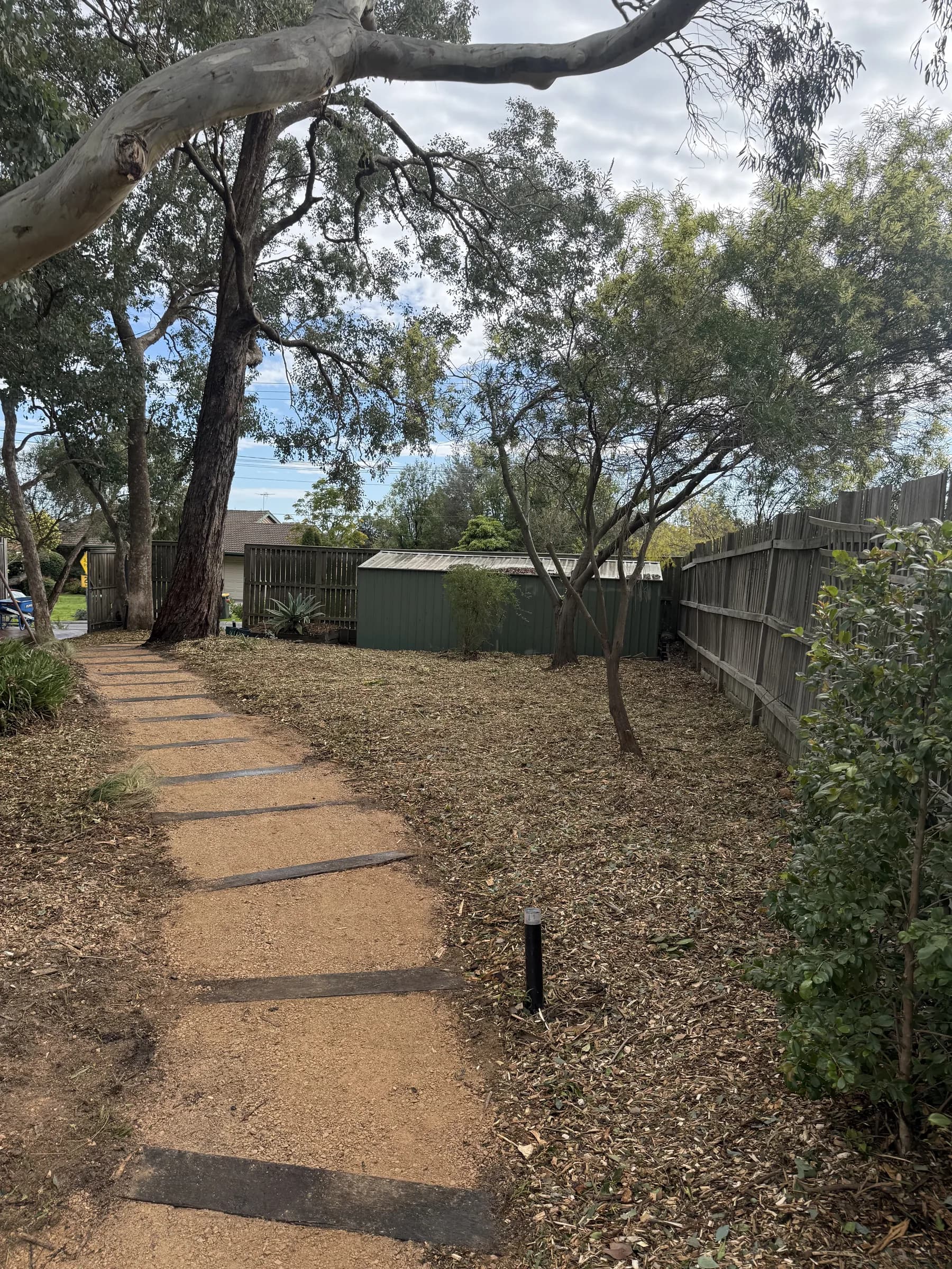 Mulched garden beds either side of a gravel path with timber sleeper steps