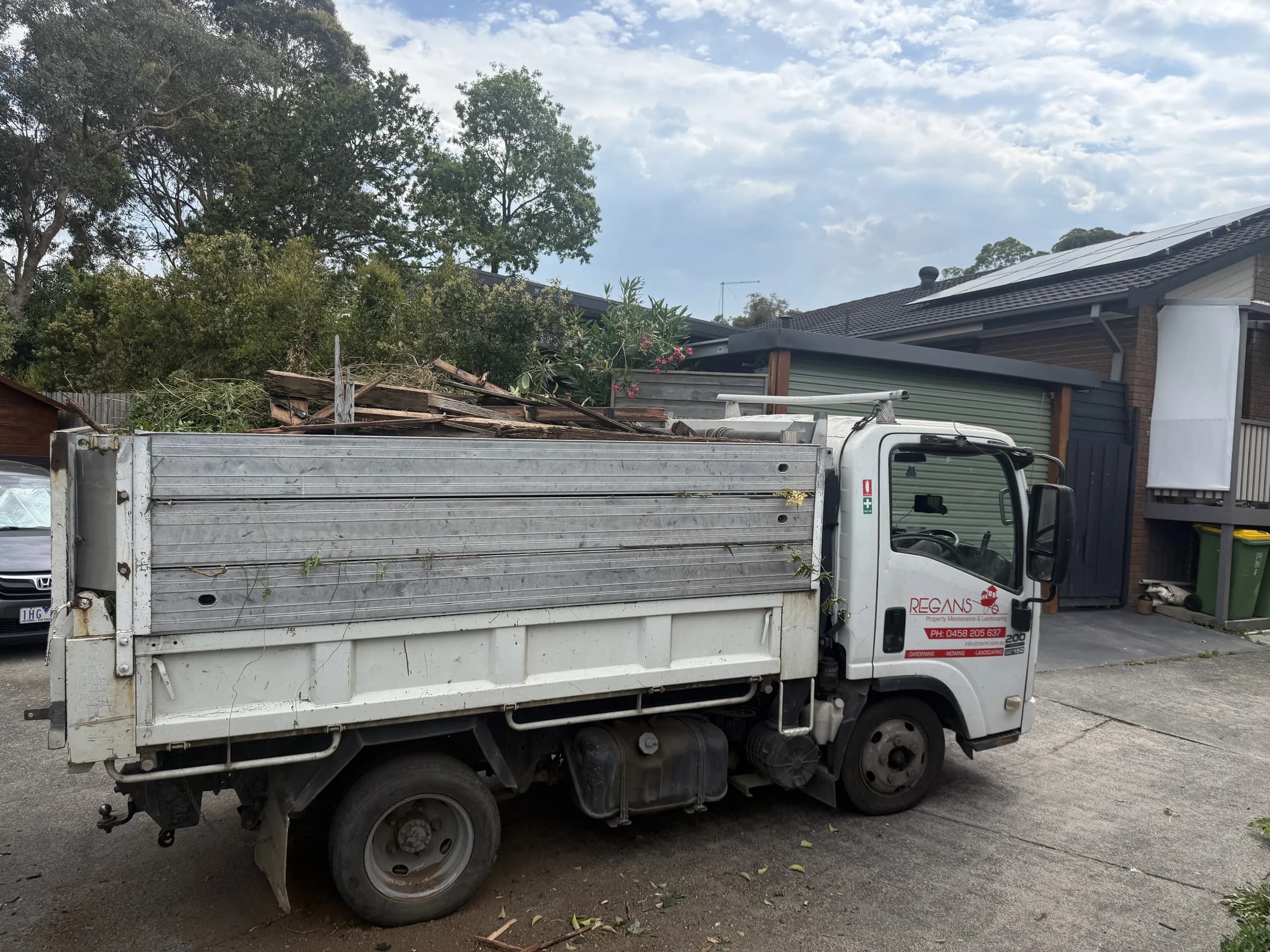 Regan's tipper truck parked in a driveway, loaded with branches and sawn timber