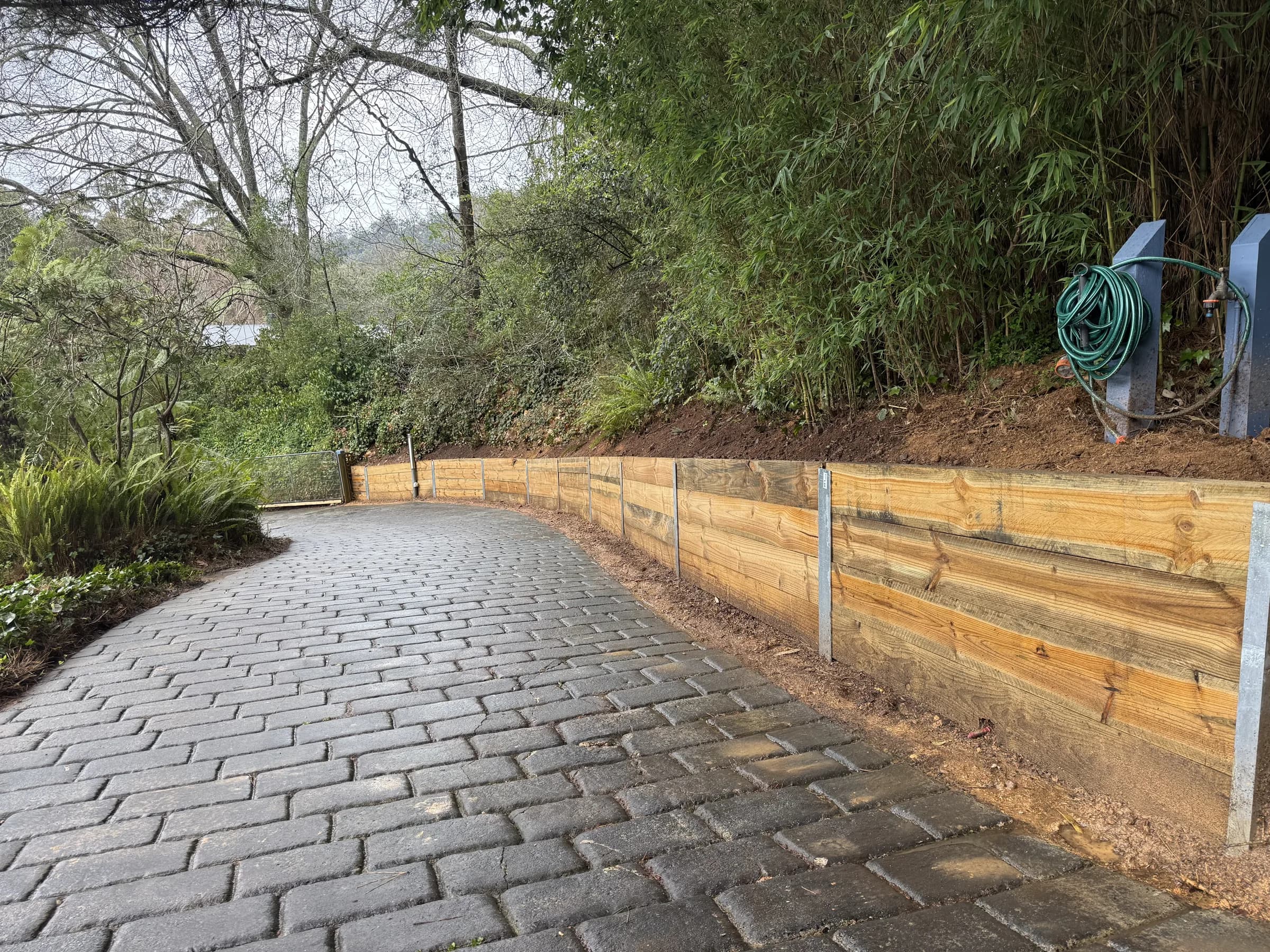 Curved timber sleeper retaining wall beside a paved driveway