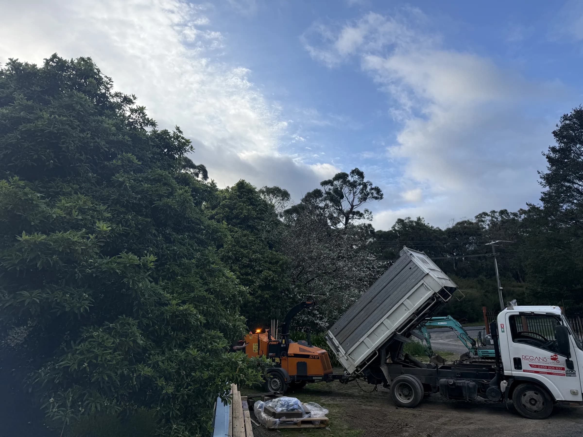 Regan's tipper, wood chipper and excavator on site at dusk