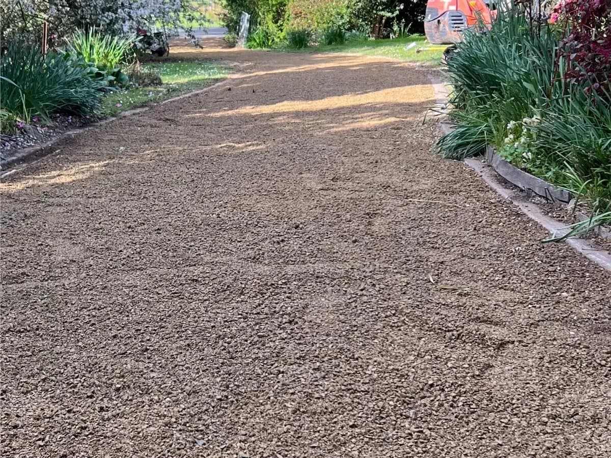 The same driveway resurfaced in crushed rock, the fresh surface running between planted garden beds to a lawn beyond