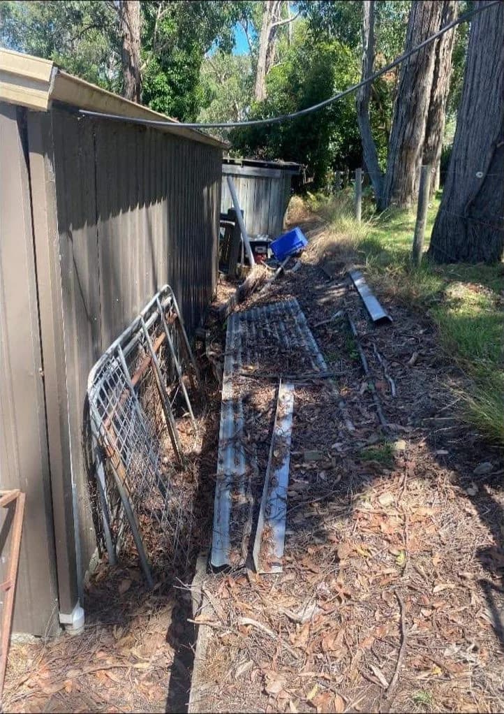 Sloping side yard beside a shed, cluttered with old gates and scrap metal