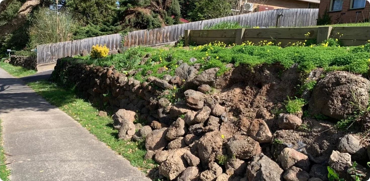 Loose rock wall along a footpath, slumping into weeds and overgrowth