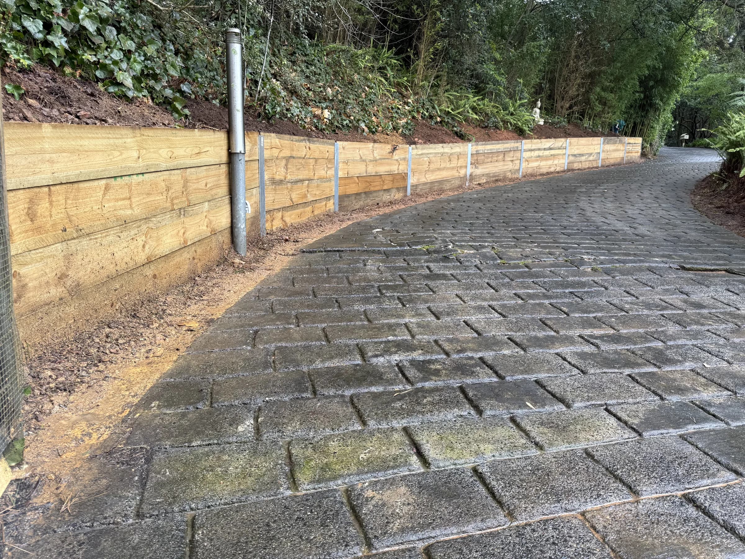 New timber sleeper retaining wall running alongside a paved brick driveway